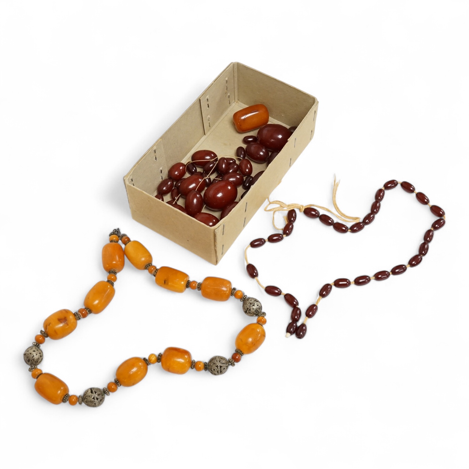 A single strand amber bead necklace, with filigree metal spacers, 48cm, gross 84 grams, together with a group of loose graduated simulated cherry amber beads, gross weight 117 grams.